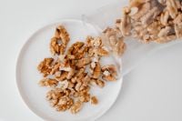 Kaboompics - Walnut Halves Spilling from a Paper Bag onto a White Plate, Snack Still Life