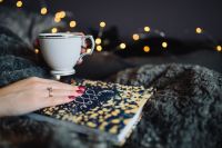Kaboompics - Hand Resting on a Hygge Book Beside a White Cup and Fairy Lights