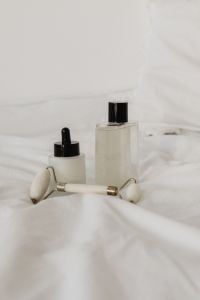 Kaboompics - Frosted Skincare Bottles and Jade Roller on Soft White Linen