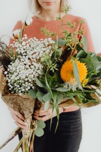 A woman holds many different flowers and leaves in her arms