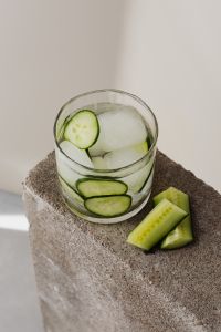 Kaboompics - High-Angle Cucumber and Lime Detox Water with Ice, Fresh Cucumber Spears on a Rough Stone Block, Vertical Summer Drink Photo
