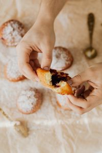 Kaboompics - Hands Breaking Open a Cherry-Filled Polish Paczki beside Powdered Doughnuts