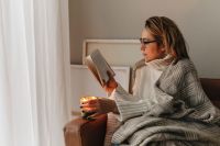 Kaboompics - Woman Reading a Book Under a Blanket by Candlelight