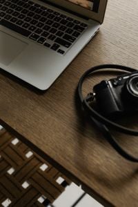 Kaboompics - Close-Up of Laptop Keyboard and Camera Strap on Wooden Desk