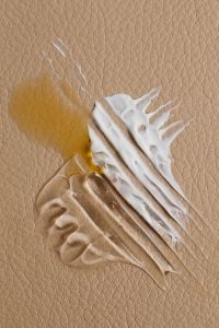 Kaboompics - White Cream Burst with Amber Swatch on Tan Pebbled Surface, Skincare Macro