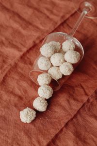 Kaboompics - Raffaello-Style Coconut Truffles Spilling from a Tipped Glass onto Rust Linen, Dessert Still Life