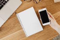 Kaboompics - Hand Holding Smartphone Beside Laptop and Blank Notebook on a Wood Desk