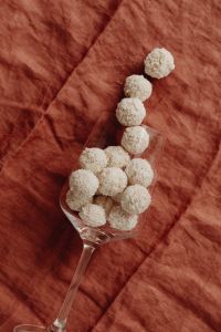Kaboompics - Coconut Truffles Spilling from a Tilted Glass onto Rust Linen, Vertical Homemade Candy Still Life