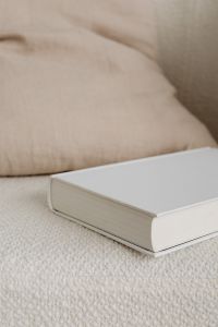 Kaboompics - Blank White Book on Cream Armchair and Linen Cushion, Vertical Mockup