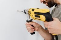Kaboompics - Handyman Drilling a Hole in a White Wall with a Yellow Power Drill, Close-Up