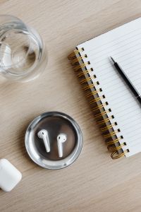 Kaboompics - Close-Up of AirPods, Notebook and Glass of Water on Desk