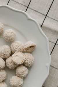 Kaboompics - Coconut Truffles and Cut Cross-Sections on a White Plate, Black-Grid Linen Dessert Flat Lay