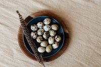 Kaboompics - Overhead Speckled Eggs on a Navy Plate with Feather, Wooden Board Easter Still Life