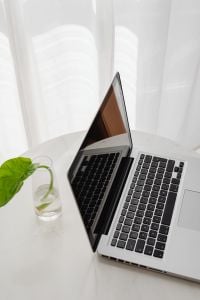 Kaboompics - Open Laptop and Green Plant in Glass on a White Desk, Remote Work by Sheer Curtains