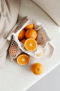 Kaboompics - Overhead Mesh Grocery Bag with Oranges and Cut Citrus on Textured Linen