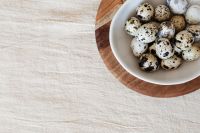 Kaboompics - Speckled Eggs in a White Bowl on Wood with Left Copy Space, Neutral Easter Recipe Background