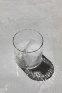 Kaboompics - Glass of Ice Water with Large Ice Cubes on White Surface, Sunlit Shadow and Minimal Background