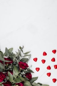 Kaboompics - Vertical Valentine's Day Flat Lay of Burgundy Flowers and Scattered Red Heart Pralines on White Marble with Copy Space
