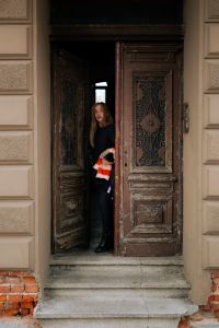 Kaboompics - Woman Peeking Through an Open Carved Door in Black Streetwear and Striped Coat