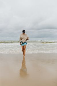 Kaboompics - Young Woman Reading a Book While Walking Along the Shore, Cloudy Beach Lifestyle Portrait