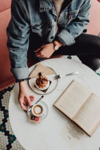 Kaboompics - A woman eats meringue, drinks coffee and reads a book in a patisserie