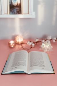 Kaboompics - Open Book beneath Cotton Stems and Candlelight on a Pink Desk