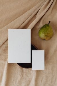 Kaboompics - Green Pear and Blank Business Card Mockup on Beige Linen with Dark Wood Plate