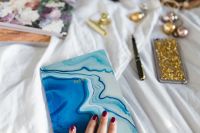 Kaboompics - Hand Holding A Blue Marble Diary On A Soft White Bed
