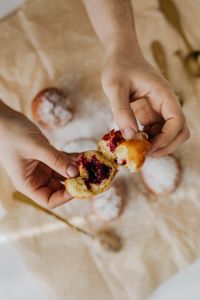 Kaboompics - Close Crop of Hands Opening a Polish Paczki to Reveal Cherry Jam on Cream Linen