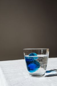 Kaboompics - Glass of Water with Blue Color Swirl Against Dark Neutral Wall, Hydration Campaign