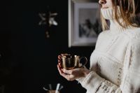 Kaboompics - Woman Holding a Gold Coffee Cup in a Cozy Knit Sweater, Dark Home Coffee Moment