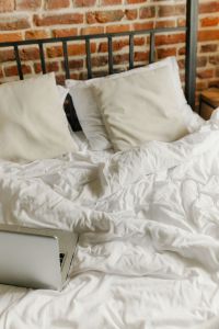 Kaboompics - Unmade White Bed with Laptop and Brick Wall, Cozy Bedroom Background