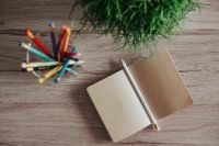 Kaboompics - Small notebooks with colourful pencils in a jar on a wooden desk