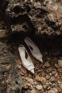 Kaboompics - Sculptural White Buckle Mules in a Rocky Shoreline Alcove