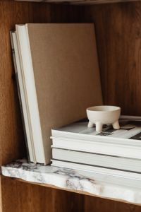 Kaboompics - Stacked Neutral Books and a Footed Ceramic Bowl on a Marble Shelf