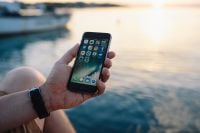 Kaboompics - Smartphone Screen Above a Seated Man's Knee with Boats on the Horizon