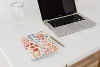 Kaboompics - Laptop Workspace with Glass of Water and Floral Notebook on Marble Desk
