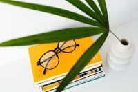 Kaboompics - Yellow Book and Eyeglasses beneath Palm Fronds, Minimalist Reading Still Life with White Vase