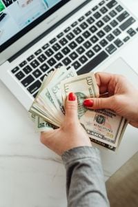 Kaboompics - Woman Counting US Dollar Bills Beside Laptop