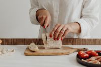 Kaboompics - Woman Cutting Rustic Bread with Tomatoes and Prosciutto
