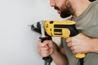 Kaboompics - Man Drilling into a White Wall with a Yellow Power Drill, Home Renovation Close-Up