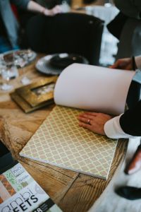 Kaboompics - Hands Unrolling Gold Geometric Wallpaper Sample on a Rustic Table
