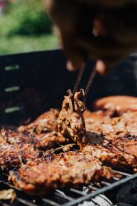 Kaboompics - Portrait Barbecue Scene with a Hand Turning Grilled Pork Neck using Metal Tongs
