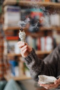 Kaboompics - Smoldering Sage Bundle Held Upright before Blurred Bookshelves