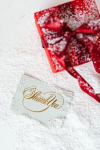 Kaboompics - Red Christmas Gift and Gold Thank You Card on a Snow-Dusted White Background