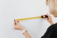 Kaboompics - Woman Measuring a White Wall with a Yellow Tape Measure for a Home Renovation Project