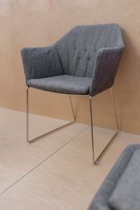 Kaboompics - Gray Tufted Upholstered Chair with Chrome Sled Legs Against a Pale Wood Wall