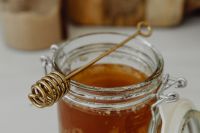 Kaboompics - Horizontal Macro of a Coiled Metal Honey Dipper over an Open Jar, Amber Honey Detail