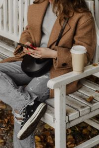 Kaboompics - Close-Up of Hands Using Phone Beside Coffee on a White Bench