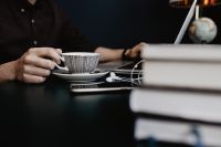 Kaboompics - Close-Up Cappuccino at Desk beside Books with Man and Laptop in Soft Focus
